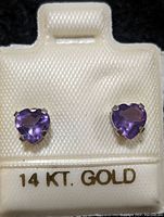 Front view of pair of heart-shaped amethyst earrings set in 14K gold displayed on white card