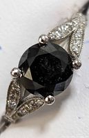 Front view showing round black diamond in four-prong setting and split shank with pave white diamonds