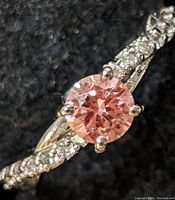 Close-up view of round pink center stone in four-prong setting with twisted pavé diamond band