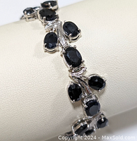 Close-up of the sterling silver natural blue sapphire bracelet showing the faceted oval and pear-shaped sapphires and leaf design detail.