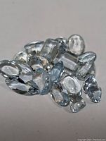 Photo of multiple loose genuine aquamarine gemstones in light blue color and various shapes.