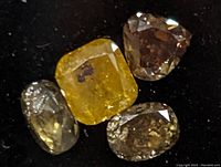 Close-up image of four assorted fancy diamonds on black background showing color and cut variations.