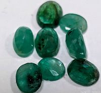 Seven genuine emerald gemstones arranged together showing color and shape variation