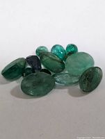 Loose emerald gemstones displayed against white background in close-up showing details of stones.