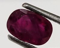 Close-up photo of the oval genuine ruby gemstone showing the deep red color and faceted polish.