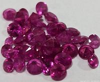 Close-up image of multiple small loose faceted ruby gemstones on a white background showing their red and purplish hues and clarity.