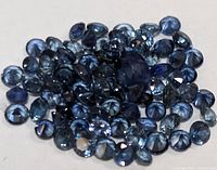Close up of multiple small faceted blue sapphires grouped together on a flat surface.