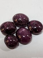 Five polished star ruby cabochon gemstones arranged on a white background showing their color, cut, and star effect.
