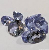 Loose tanzanite faceted gemstones in various cuts and shapes on a white background.