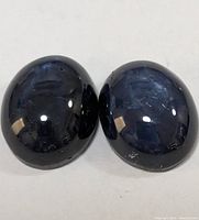 Two dark blue star sapphire cabochon gemstones side by side on white surface showing star effect and polish.