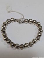 Full view of the silver bead bracelet arranged in a circular manner, showing the large spherical beads and lift-clasp closure.