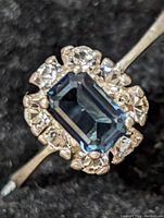 Close-up image of the ring showing the rectangular blue central stone surrounded by clear stones and slender silver band.