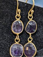 Front view of earrings showing faceted amethyst stones with silver bezel settings and hooks.