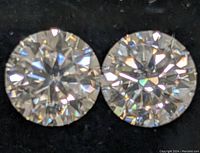 Close-up front image of two sparkly round clear Moissanite stones on a black background.