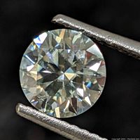 Close-up image showing the round cut moissanite gemstone held by tweezers, highlighting facets and sparkle.