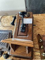 Photo of antique wooden wall-mounted telephone showing the main unit with mouthpiece, crank, brass bells, and separate earpiece on a hook.