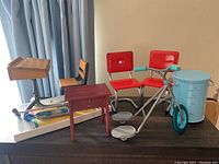 Image showing assorted American Girl doll furniture including school desk, diner chairs, tricycle, and blue multi-drawer cabinet.