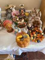 All assorted seasonal decorations on a white tablecloth including Halloween, Fall, Easter items such as bunnies, a turkey, pumpkins, and a wreath.