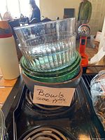 Photo showing stack of five glass bowls including Pyrex with a label board saying 'Bowls some pyrex'. Bowls vary in clear and green ribbed glass.