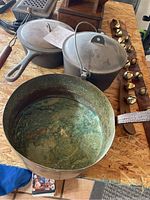 Photo showing three cast iron pots including skillet, lidded pot with bail handle, and a deep pot with fixed handle exhibiting patina.