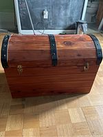 Closed cedar chest showing dome lid with black metal bands and brass-colored clasps on front.