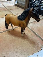 Brown standing horse figurine with black mane and tail with realistic detailing on a tile floor.