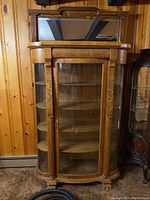 Front view of large wooden china cabinet with curved glass door and visible shelves inside