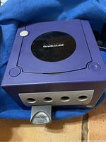 Purple Nintendo GameCube console cube shape with 4 controller ports on front. Controller plugged in visible.