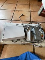 Photo showing Nintendo Wii console, Wii Fit Board, Wii Remote, power adapter and composite AV cables all tangled together on tile floor.