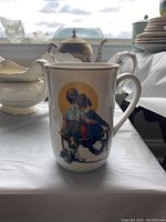 Photo of one cup showing a Norman Rockwell illustration of a boy and girl seated with a dog, cream background with gold rim on top.