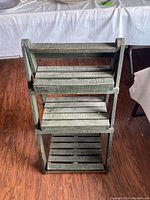Front view of the three-tier green wooden plant stand showing slatted shelves and textured finish