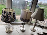 Photo showing three distinct table lamps on a window sill with outdoor background.