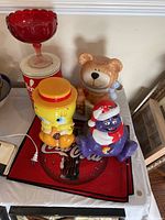 Photo showing Tweety Bird, bear, purple Santa cookie jars, Coca-Cola tin, placemats, and red scalloped glass pedestal bowl