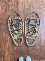 Pair of vintage snow shoes on wooden floor showing full frames and leather straps