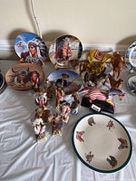 Wide view of the lot arranged on a table showing several decorative plates with Native American and Western themes, various horse figurines, and some miniature bottles in front.