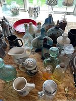 Wide view showing assortment of whiskey bottles and glassware on table, includes ceramic mugs, pitchers, and blue and green glass bottles