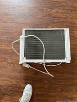 Photo of a single window unit air conditioner placed on a wood floor with power cord wrapped around it.
