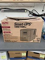 Front of box showing APC logo, Smart-UPS 1000/1500VA model name and marketing text