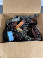 Box showing assorted curved and straight model train track pieces and multiple train cars inside.