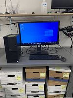 Full setup displayed on table: Dell desktop tower, connected Dell monitor powered on showing Windows desktop, keyboard and mouse placed in front, various cables connected.