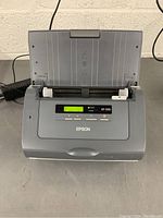 Front view of Epson GT-S50 scanner powered on showing LED indicators and display screen.