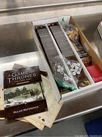 Box containing multiple decks of cards organized in trays, tokens in plastic bags, and papers for A Game of Thrones: The Card Game.