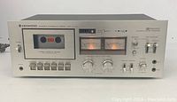 Front view of Kenwood stereo cassette deck model KX-1030 showing cassette window with tape inside and illuminated VU meters, front control buttons and knobs.