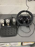 Logitech G920 racing wheel and three-pedal base set shown together with cables attached.