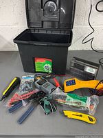 Overall view of all electrician tools on table with black plastic storage container.