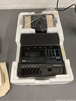Panasonic cassette transcriber device inside original styrofoam packaging with some accessories and documentation visible.