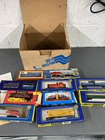 Photo showing assorted boxed model train cars and locomotives on a table with original packaging next to a cardboard box.