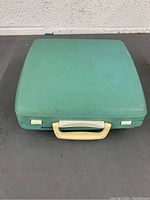 Top view of closed teal hard case with white handle and latches for portable typewriter