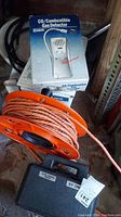 Overview of gas detector box, orange extension cord reel, and box of tapes in garage.
