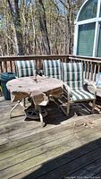 Full view of four green and white striped chairs surrounding round glass top table covered with a fabric cover on a wooden deck.
